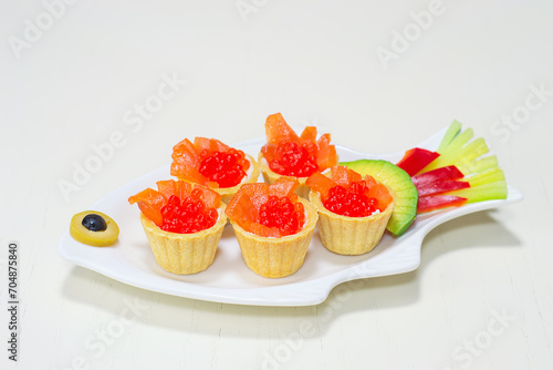 Red caviar and pieces of salmon, in tartlets on a white plate. Selective focus