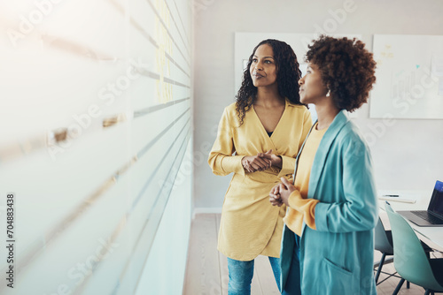 Businesswomen brainstorming together using adhesive notes on an office wall photo