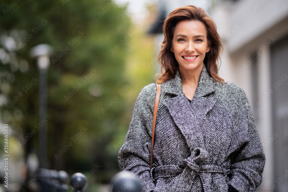 Brunette haired woman wearing tweend coat and walking outdoors in the city street on autumn day - obrazy, fototapety, plakaty 