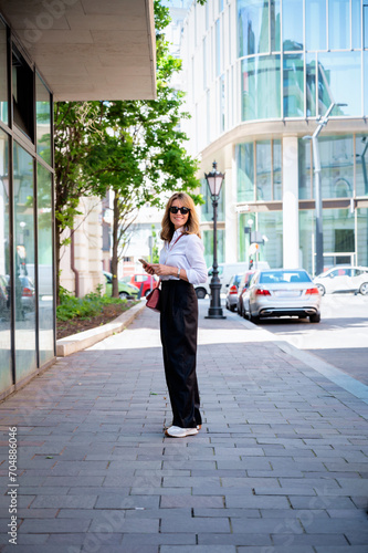 Attractive mid aged woman with smartphone walking on the street