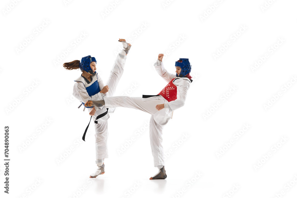 Leg kick. Young girl, competitive taekwondo athletes in dobok and helmet training isolated over white background. Concept of martial arts, combat sport, competition, action Leg kick. Young girl, competitive taekwondo athletes in dobok and helmet training isolated over white background. Concept of martial arts, combat sport, competition, action