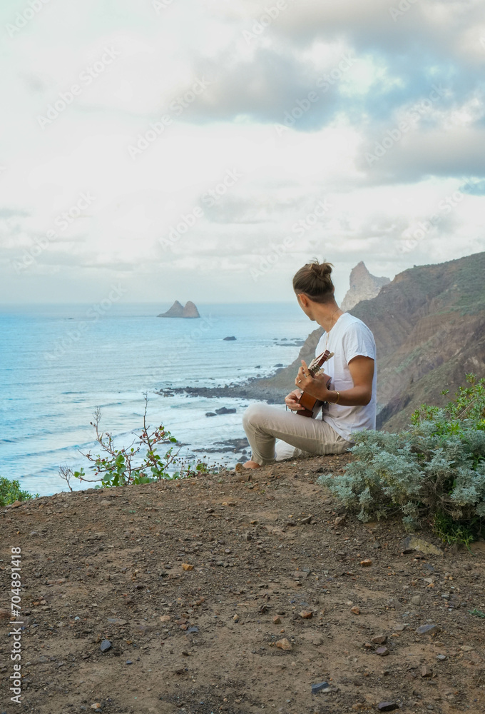 Harmony with Nature: Unrecognizable Young man Playing Guitar on a Cliff, Overlooking the Ocean and Rugged Cliffs, Captured in Natural Light
