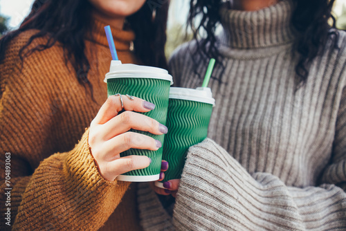 Close-up shot of two people holding green textured takeaway cups with straws, clad in cozy knitted sweaters, embodying the warmth of friendship and autumn