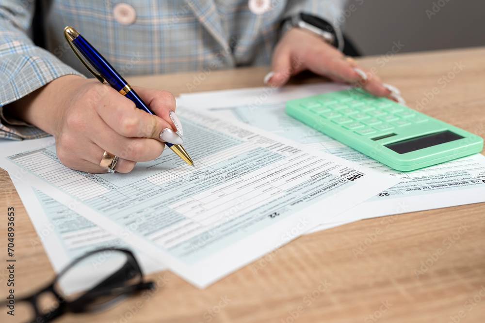 Female hand using calculator for fill 1040 tax form business individual income at office Female hand using calculator for fill 1040 tax form business individual income at office