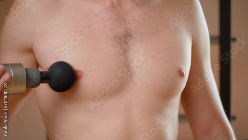 A guy gives himself a self-massage of the pectoral muscle with a percussion massager, close-up. Chest massage after training photo