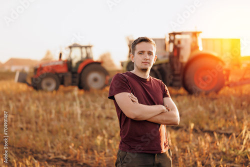 Portrait young man farmer in cornfield background harvester and tractor on harvested corn, sunlight. Concept Farm small business agricultural photo