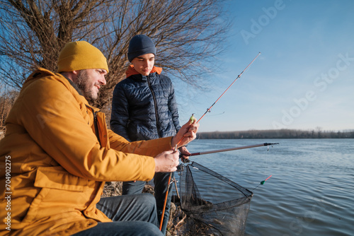 Father and son are fishing on sunny winter day. Freshwater fishing. Teenage boy is learning to fish.