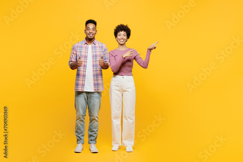 Full body young couple two friend family man woman of African American ethnicity wear purple casual clothes together point index finger aside on area show thumb up isolated on plain yellow background