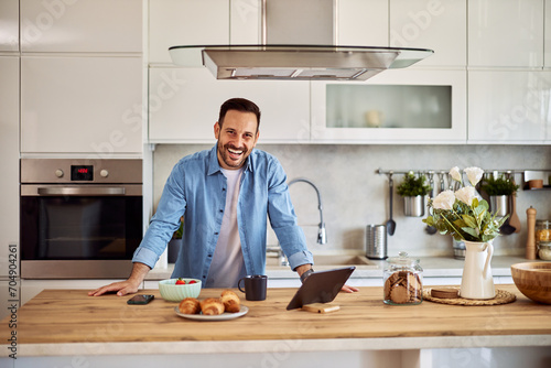 Portrait of a cheerful male online content creator leaning on his hands on a kitchen counter with breakfast in front of him. photo