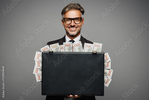 Adult rich happy employee business man corporate lawyer he wears classic formal black suit shirt tie work in office hold of cash money in case for dollar banknotes isolated on plain grey background.