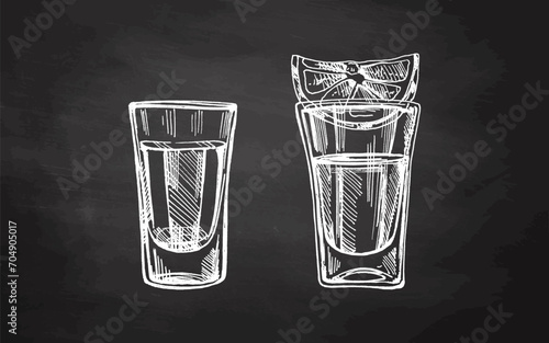 Hand-drawn shot glasses with tequila with a slice of lime on chalkboard background. Design element for the menu of bars and restaurants. Mexican, Latin America.