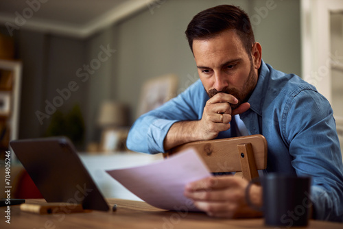 A focused young adult male freelancer analyzing the documents in his hand with a hand over his mouth. photo