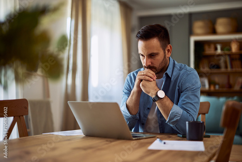 Foto A deep-in-thought male freelance writer revising his latest work on a laptop with his hands connected on his chin