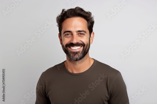 Portrait of a happy young man smiling and looking at camera against grey background © Inigo