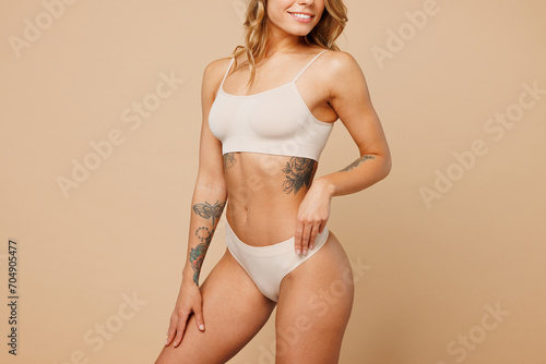 Cropped close up young nice lady woman with slim body perfect skin wearing nude top bra lingerie stand put hand hold thighs isolated on plain pastel light beige background. Lifestyle diet fit concept.