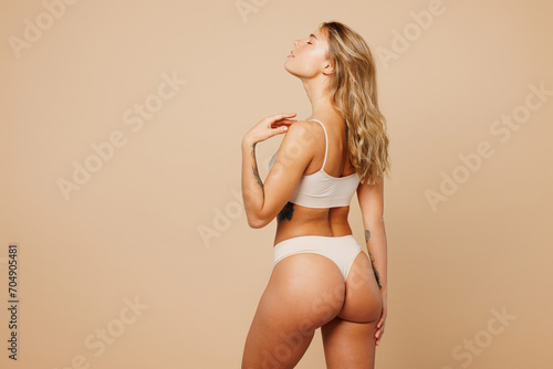 Back rear view young nice lady woman with slim body perfect skin wear nude top bra lingerie stand close eyes touch herself isolated on plain pastel light beige background. Lifestyle diet fit concept.