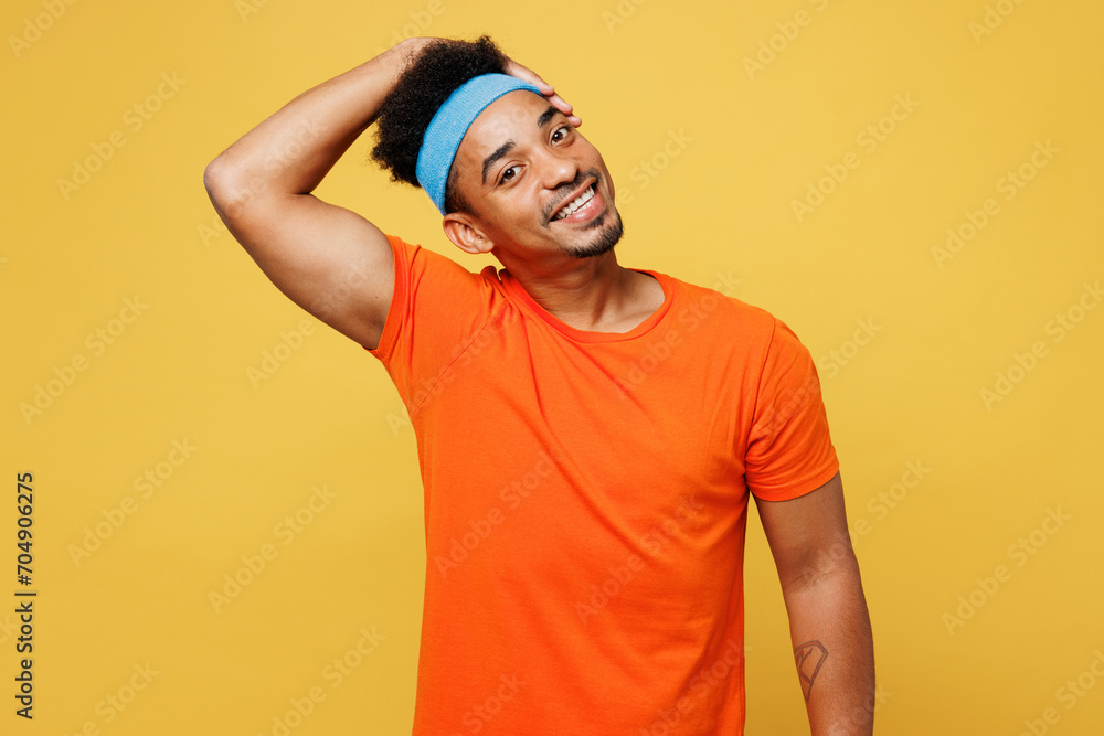 Young fitness trainer instructor sporty man sportsman wear orange t-shirt tilting hold his head look camera spend time in home gym isolated on plain yellow background. Workout sport fit abs concept. Young fitness trainer instructor sporty man sportsman wear orange t-shirt tilting hold his head look camera spend time in home gym isolated on plain yellow background. Workout sport fit abs concept.