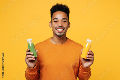 Young smiling fun man wear casual clothes hold show fruit juice green vegetable smoothie as detox diet isolated on plain yellow background. Proper nutrition healthy fast food unhealthy choice concept.