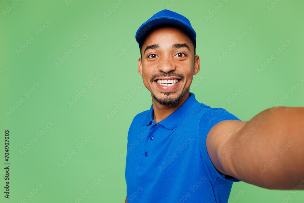 Close up professional delivery guy employee man wear blue cap t-shirt uniform workwear work as dealer courier do selfie shot on mobile cell phone isolated on plain green background. Service concept. Close up professional delivery guy employee man wear blue cap t-shirt uniform workwear work as dealer courier do selfie shot on mobile cell phone isolated on plain green background. Service concept.