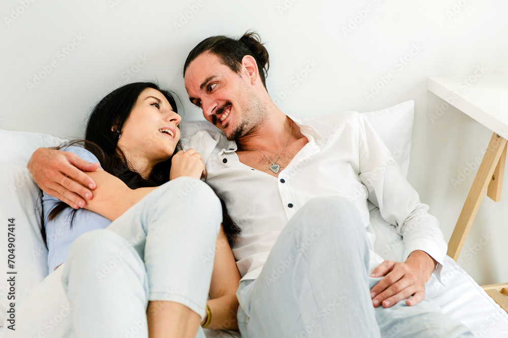 Happy smiling Caucasian couple lying on a comfy bed, relaxing and looking each other in the eyes and smiling. Romantic couple in love looking at each other. Couple spend quality time in a relationship Happy smiling Caucasian couple lying on a comfy bed, relaxing and looking each other in the eyes and smiling. Romantic couple in love looking at each other. Couple spend quality time in a relationship