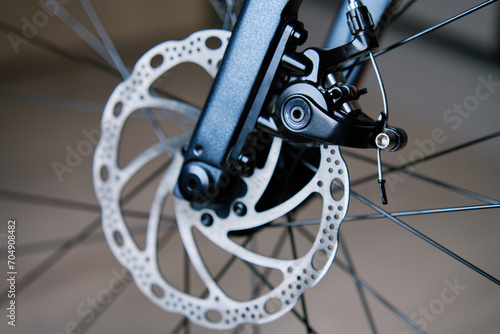 Part of the bicycle's braking system. Grey metal brake disc and brake pads on road bike, close up.