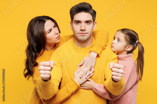 Young sad parents mom dad with child kid girl 7-8 years old wear pink knitted sweater casual clothes hold car like driving, hug pov safety belt isolated on plain yellow background. Family day concept.