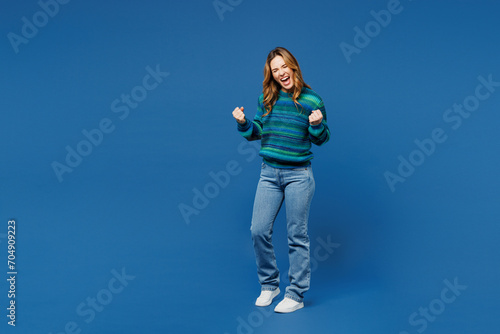 Full body young woman she wears knitted sweater casual clothes doing winner gesture celebrate clenching fists say yes isolated on plain blue cyan color background studio portrait. Lifestyle concept.