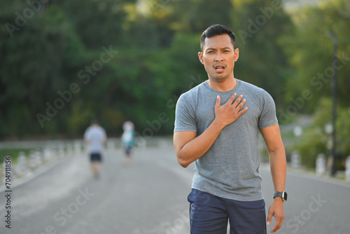 Tired sportsman touching his chest feeling pain in heart during exercise outdoor