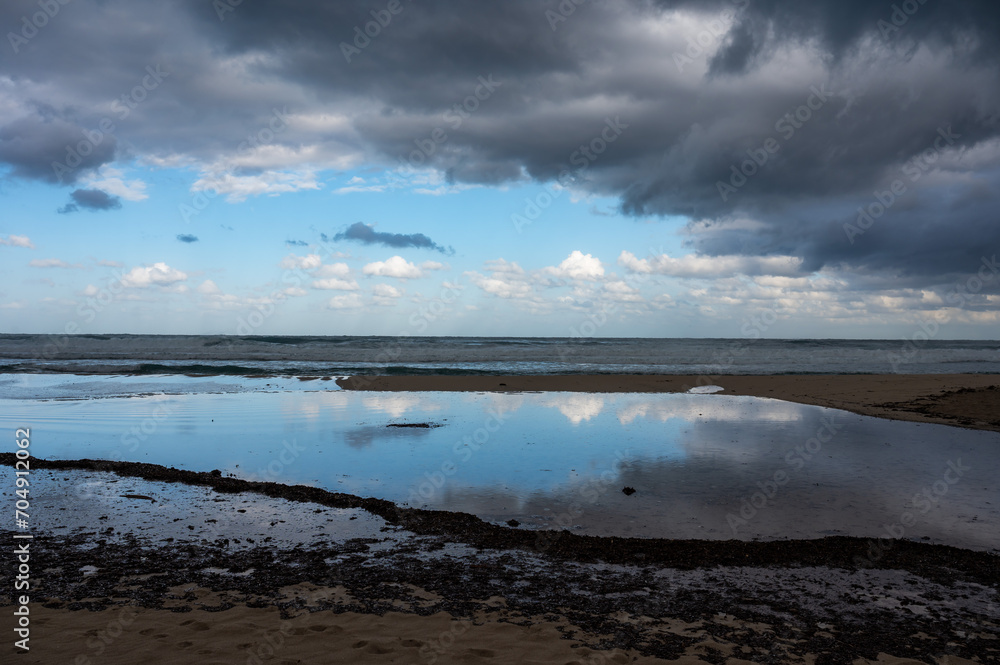 Dark rainy clouds reflecting in the water ponds at the beach of Mondello, Italy