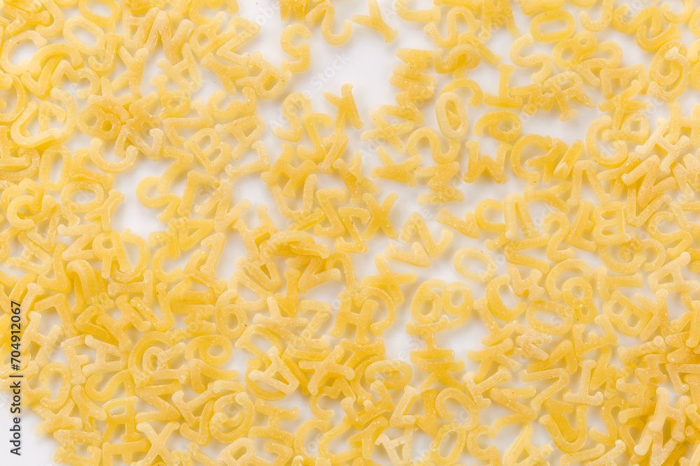 Obraz premium Raw alphabet pasta on white dish , top view close-up