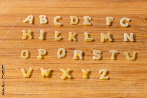 Alphabet pasta placed in alphabetical order on bamboo cutting board