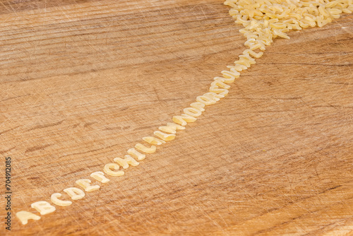 Raw alphabet pasta on cutting board lined up from heap