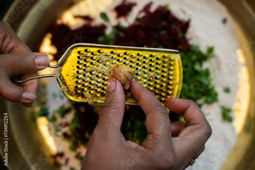 Grating ginger root with a grater in the kitchen, Grating ginger into shredded pieces, Close-up of hands with to shred ginger into a white plate,.