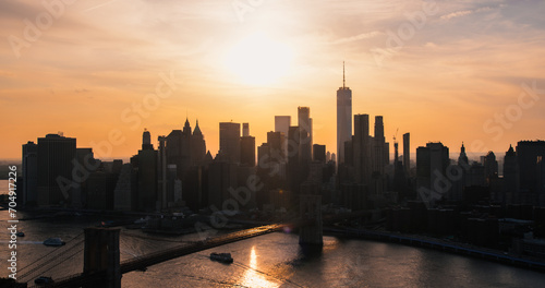 Iconic New York City Landscape Over East River with Skyscrapers, Brooklyn Bridge, Cars and Ferry Boats. Cinematic Evening Urban Skyline with Sunset and Lightly Clouded Sky