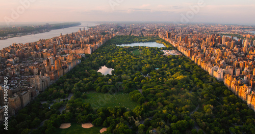 Fototapeta Naklejka Na Ścianę i Meble -  New York Cityscape at Sunset. Aerial Shot from a Helicopter. Modern Skyscraper Buildings Around Central Park in Manhattan Island. Focus on Nature, Trees and Lakes in the Park in the City
