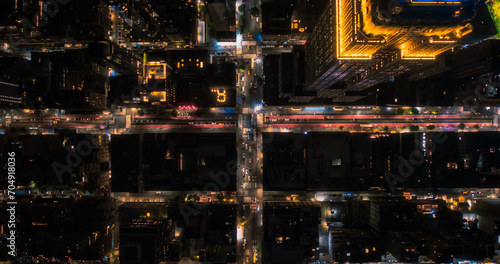 Top Down Aerial View of New York City Streets at Night with Visible Grid System, Business and Residential Building Roofs. Busy Center with Traffic, Cars, Yellow Taxis, Commercial Vehicles, Pedestrians