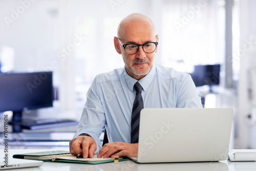 Mid aged businessman sitting in the office and having web conference