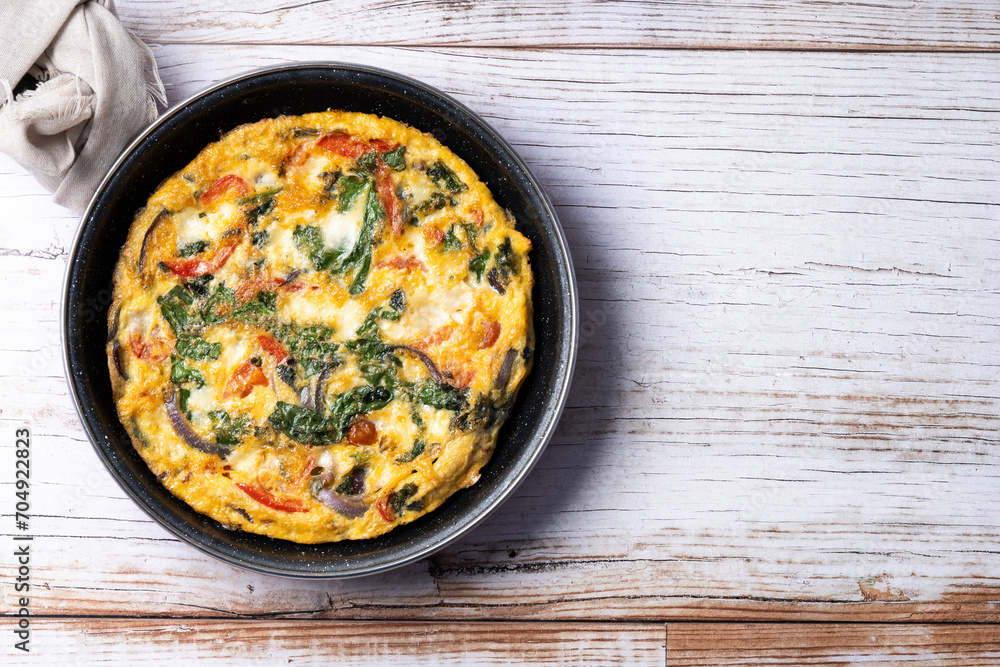 Italian Frittata made with spinach, tomatoes, onion and peppers on white wooden table. Top view. copy space Italian Frittata made with spinach, tomatoes, onion and peppers on white wooden table. Top view. copy space
