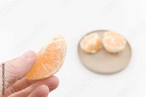immagine con primo piano di mano che regge frutti di arancia, clementina su superficie bianca