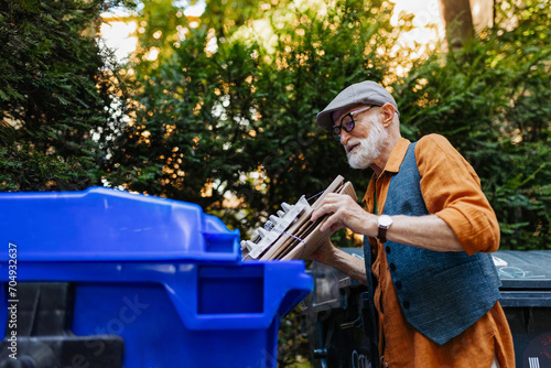 Fotografie Senior man throwing paper waste, cardboards into recycling container in front apartment