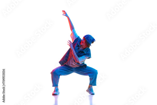 Young girl wearing casual jean clothes and head accessories dancing hip hop isolated over white background in neon light. Concept of contemporary dance, street style, youth, hobby, action, lifestyle