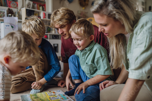 Cheerful family with three kids reading book in living room, on floor. photo