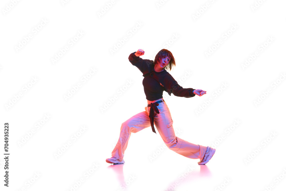 Active young girl in casual clothes dancing hip hop, dance hall isolated over white background in neon light. Concept of contemporary dance, street style, youth, hobby, action, lifestyle