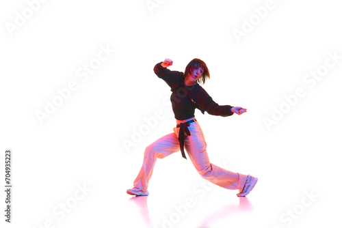 Active young girl in casual clothes dancing hip hop, dance hall isolated over white background in neon light. Concept of contemporary dance, street style, youth, hobby, action, lifestyle