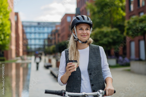 Beautiful middle-aged woman commuting through the city, buying, drinking coffe in front of office. Female city commuter traveling from work by bike after a long workday. © Halfpoint