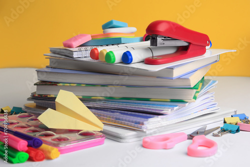 Many books, paper plane and different school stationery on white table against orange background. Back to school