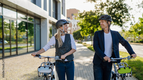 Spouses commuting through the city, talking and walking by bike on street. Middle-aged city commuters traveling from work by bike after a long workday.