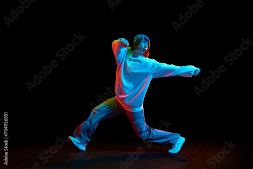 Hip hop culture. Young woman in sportive clothe dancing modern dance styles isolated over black background in neon light. Concept of contemporary dance, street style, youth, hobby, action, lifestyle