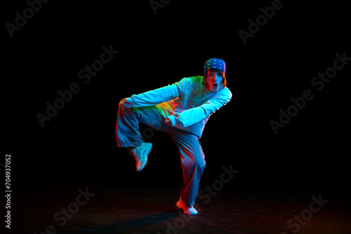Artistic young woman in sportive casual clothe dancing hip hop isolated over black background in neon light. Concept of contemporary dance, street style, youth, hobby, action, lifestyle