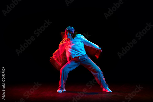 Young woman in casual clothes dancing hip hop isolated over black background in neon light with mixed lights effect. Concept of contemporary dance, street style, youth, hobby, action, lifestyle